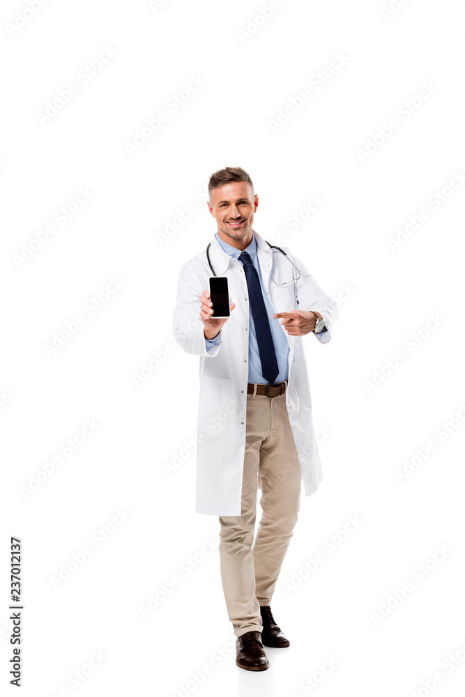 smiling doctor pointing with finger at smartphone with blank screen isolated on white smiling doctor pointing with finger at smartphone with blank screen isolated on white