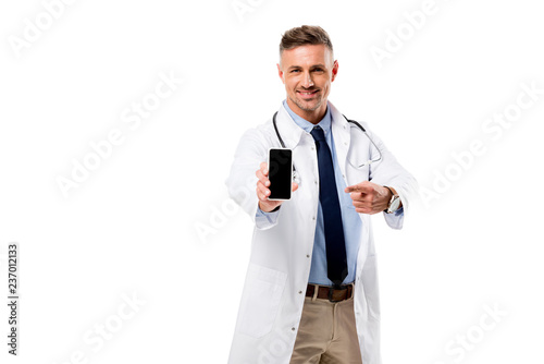 Smiling doctor pointing with finger at smartphone with blank screen isolated on white
