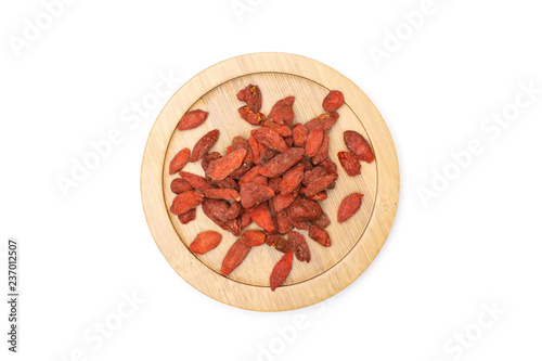 Lot of whole dried red goji berries on round bamboo plate flatlay isolated on white background