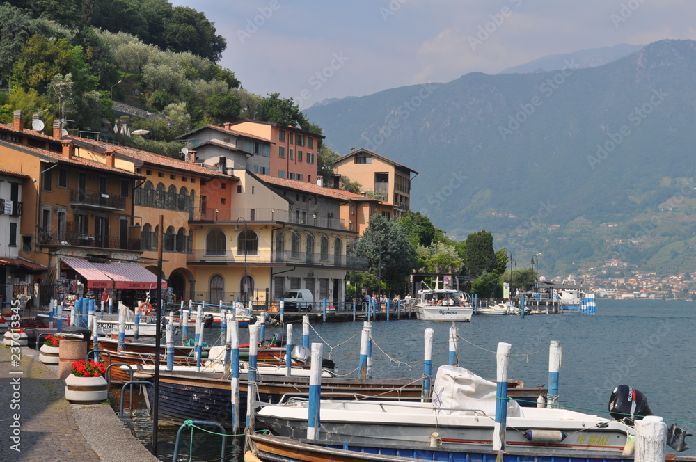 Boats at the pier, promenade, mountains and houses. Lake Iseo in Italy.