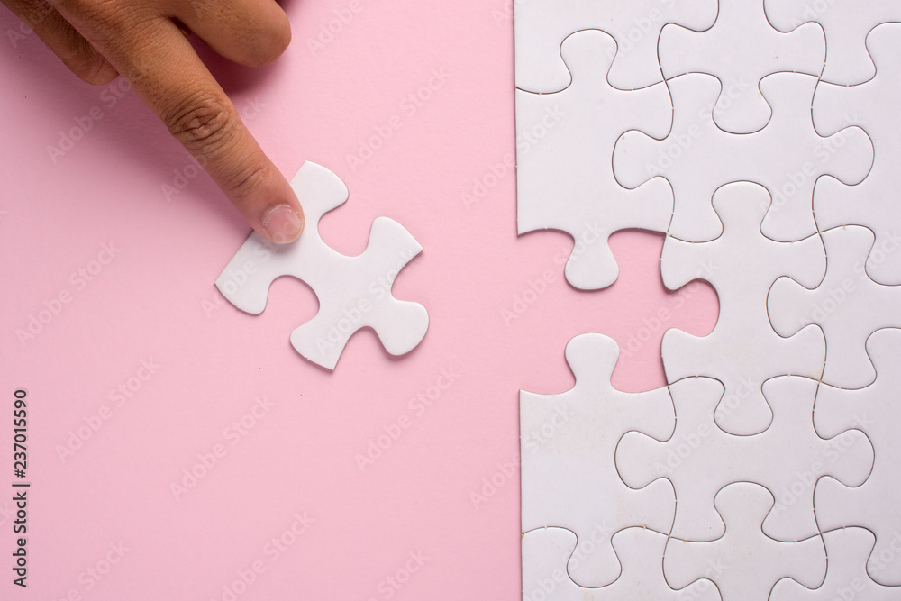 Close up of hand placing the last jigsaw puzzle piece on pink background. Business and team work concept. Close up of hand placing the last jigsaw puzzle piece on pink background. Business and team work concept.