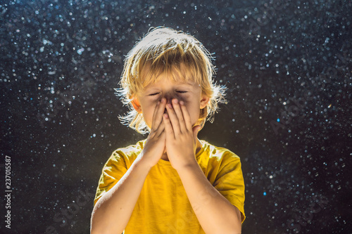 Allergy to dust. Boy sneezes because he is allergic to dust. Dust flies in the air backlit by light