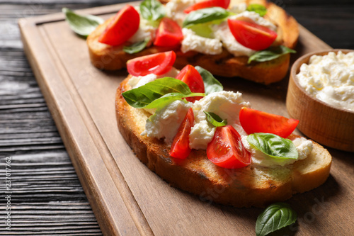 Toasted bread with tasty cream cheese and tomatoes on wooden board