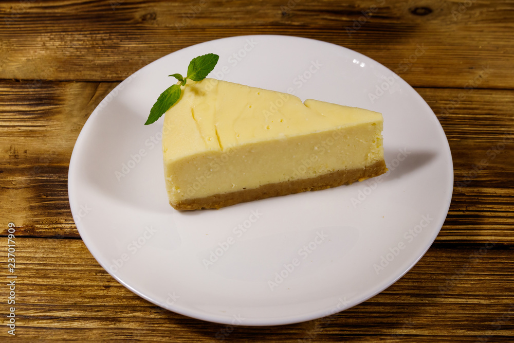 Piece of tasty sweet New York cheesecake in a white plate on wooden table