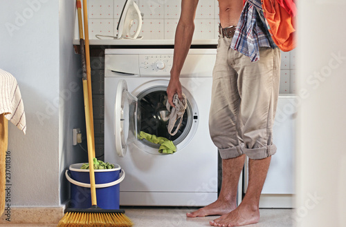 Male housewife or bachelor concept. Young man loads the laundry into the washing machine