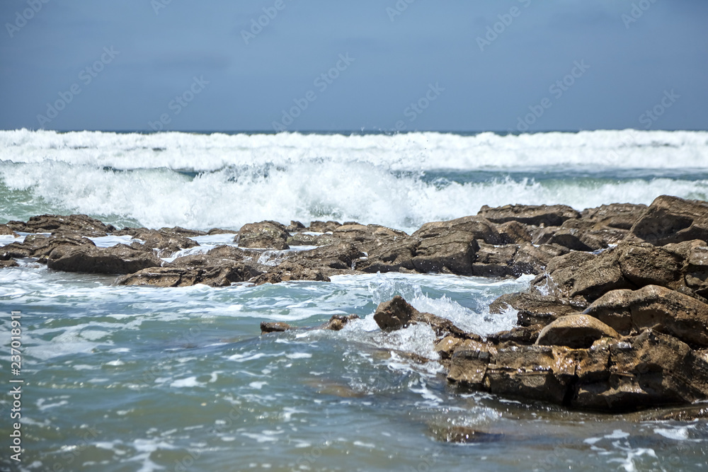 Fototapeta premium Waves crashing against a stones with foam and splashes. Ocean shore. Rocky beach