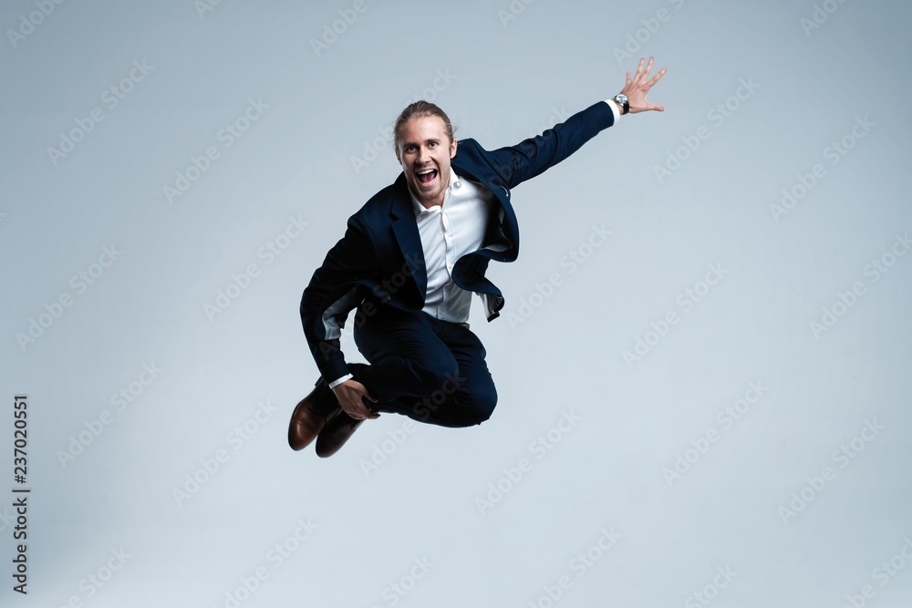 Young successful businessman in suit rejoicing, jumping over white background.
