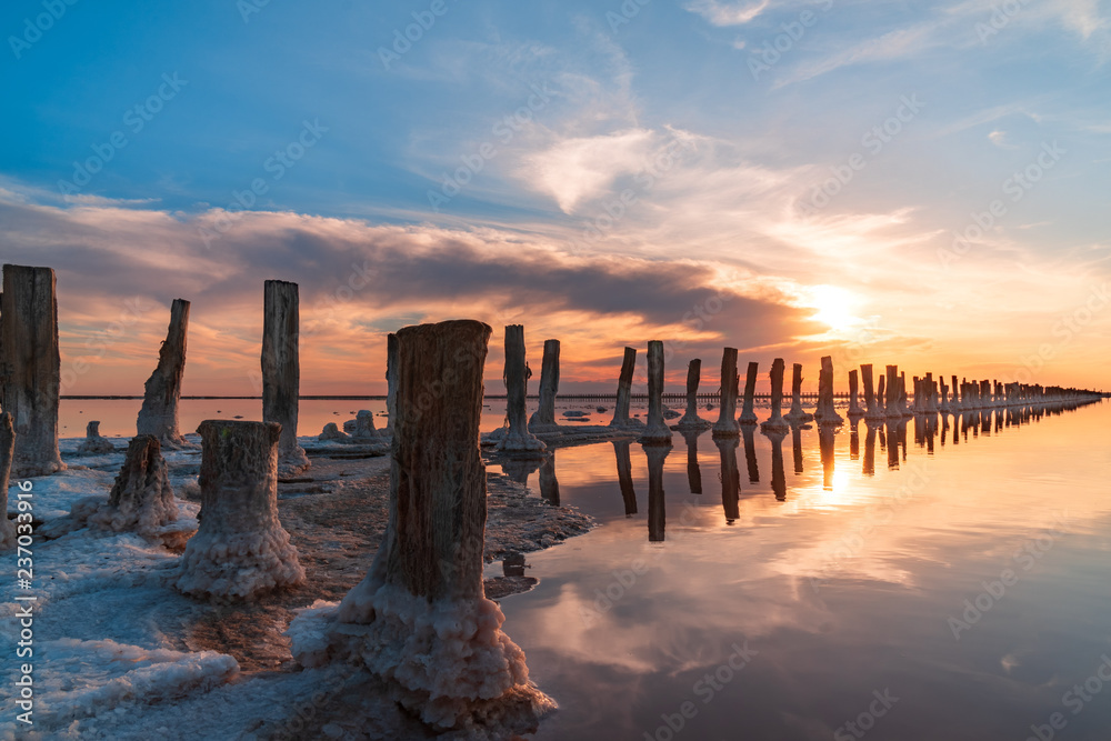 sunset on a pink salt lake, a former mine for the extraction of pink salt. row of wooden pegs overgrown with salt.