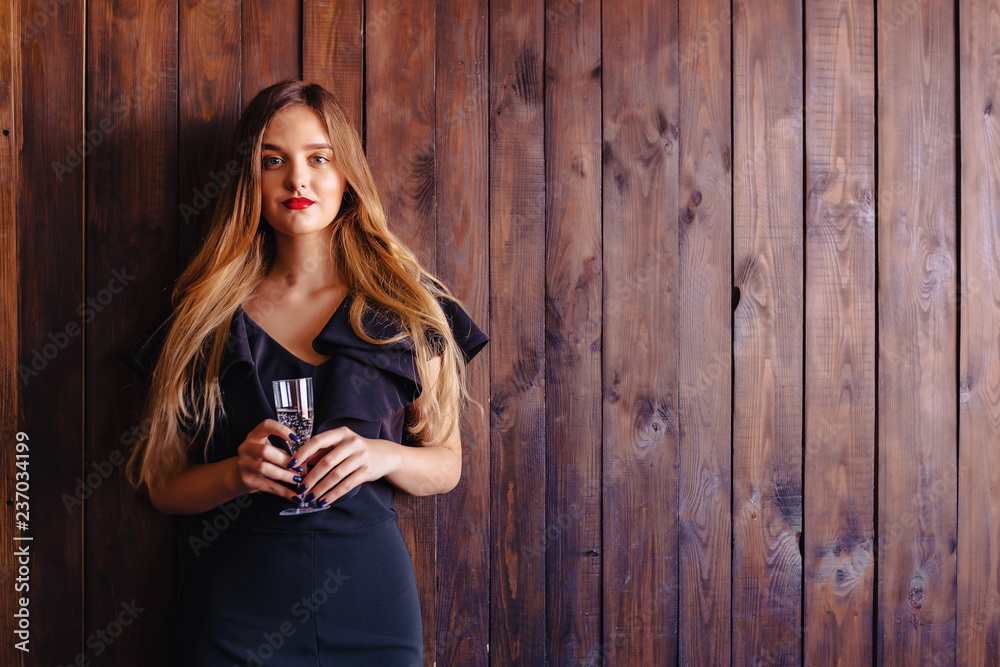 Fototapeta premium young attractive girl with a glass of champagne or wine on the background of the wall