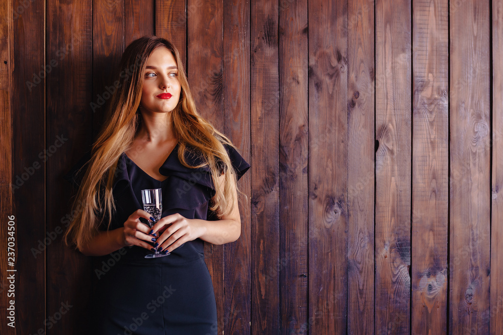 Fototapeta premium young attractive girl with a glass of champagne or wine on the background of the wall