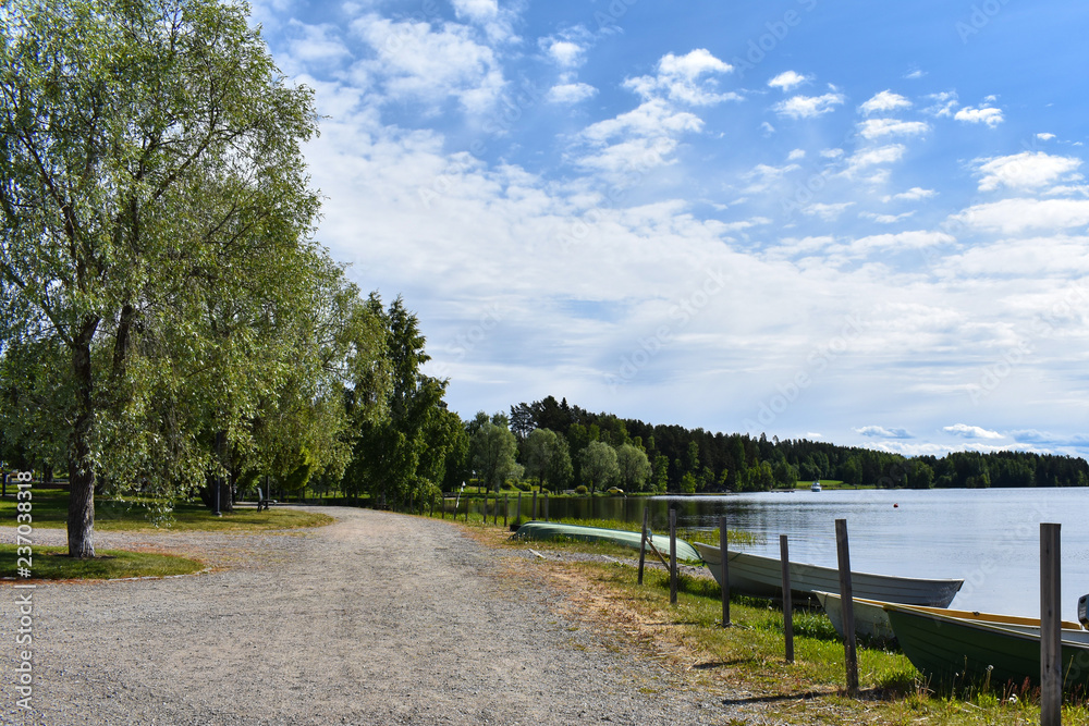 Boats parked by the lake's shore along the stony pathway with lots of trees.