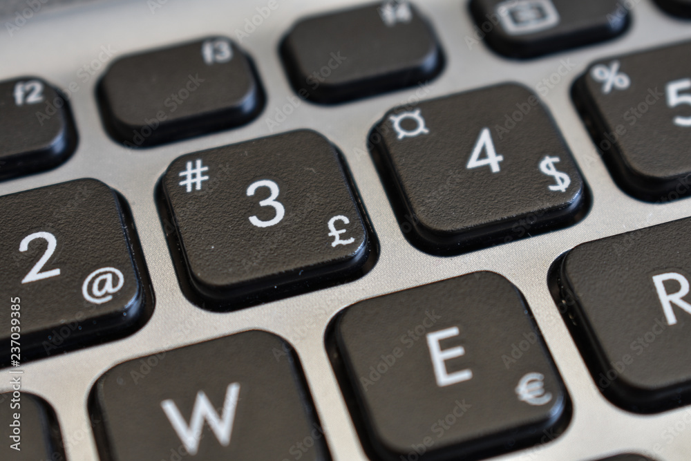 Pound sign and other symbols, letters, and numbers on a black keyboard of a gray laptop.