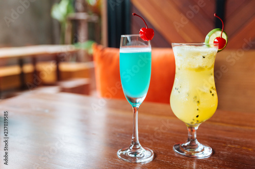 Turquoise color cocktail and passion fruit cocktail served with fresh cherry.