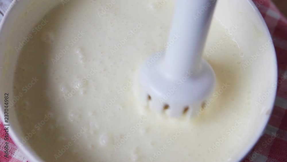A woman uses an immersion blender to combine a cream cheese mixture