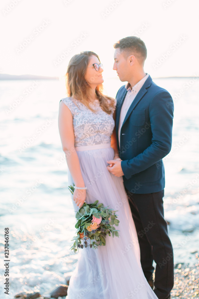 Happy groom and bride in beautiful wedding dress standing on the rocks near the Garda lake. Sirmione, Italy. Wedding couple.