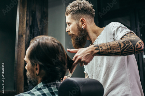Thoughtful barber looking at the mirror while touching hair of client