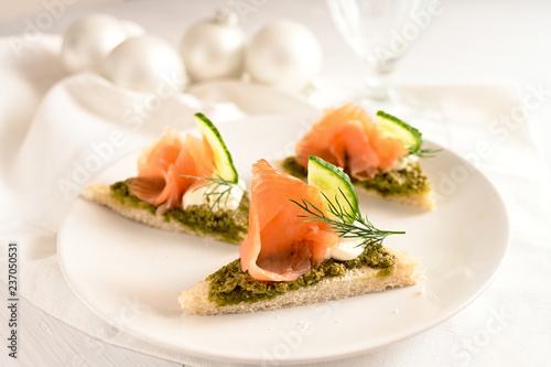 festive canapes with smoked salmon, pesto, cucumber and dill garnish, white table cloth and christmas decoration, copy space