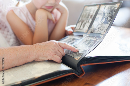 Grandmother and granddaughter watching old photo album at home. Senior woman shows child black and white photos. Hands of retired person and kid. Family leisure.