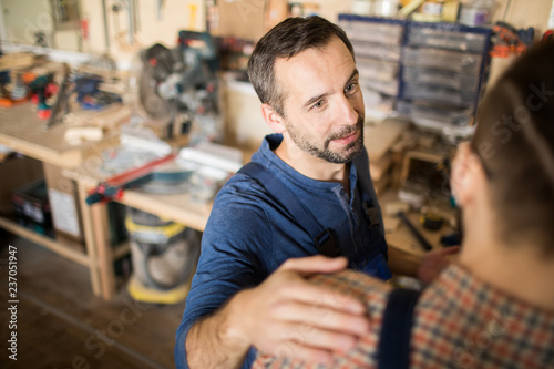 Quadro su tela High angle portrait of mature carpenter patting colleague on shoulder while work