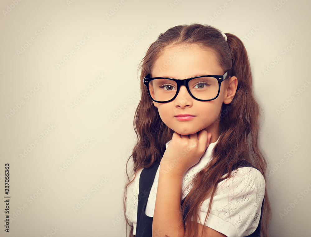 Thinking serious pupil girl with long hair style in fashion eyeglasses with hand under the face in uniform. TOned vintage portrait