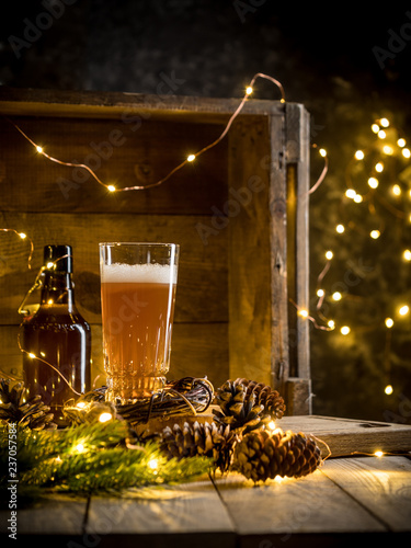 Beer in glass on wooden background with Christmas lights and pine cones