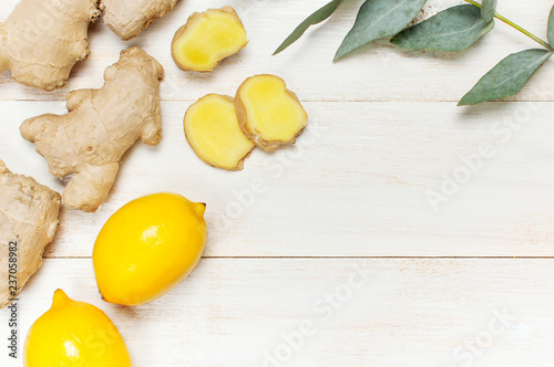 Whole and sliced fresh ginger roots, eucalyptus, lemon on white wooden background top view copy space. Seasoning, spice, ingredient for tea. Concept healthy food, medicine, improving immunity