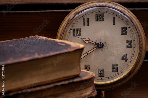 Panta rhei concept: antique pocket watch and pile of vintage hard cover books on natural stone background.