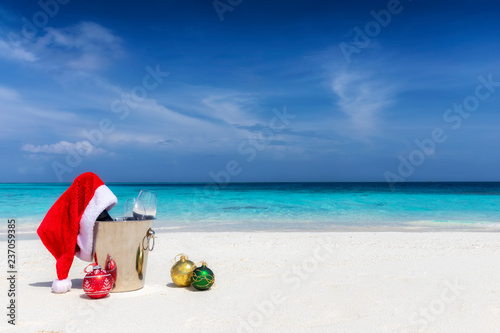 Weihnachten in der Karibik: Champagner Kübel mit roter Weihnachtsmütze und Christbaumkugeln im Sand