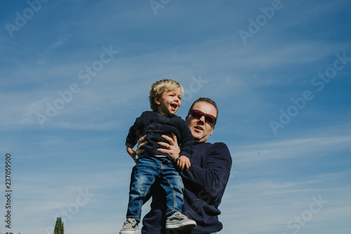 .Funny father playing with his son in the park on a sunny autumn day. Throwing him into the air, making him fly while the kid laughs. Lifestyle