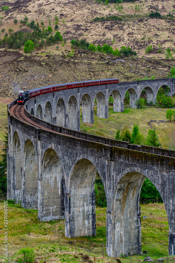 Glenfinnan Viaduct, Scotland. Travel/tourist destination in Europe. Old historical steam train riding on film scene famous viaduct bridge. Highlands, mountains, outdoor background.