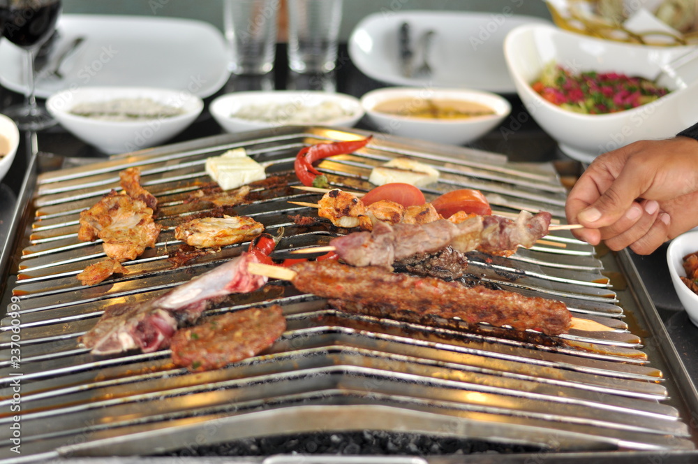 Traditional Cypriot meze and mix meat and chicken kebab table with charcoal barbecue on the table for self cooking during the eating time