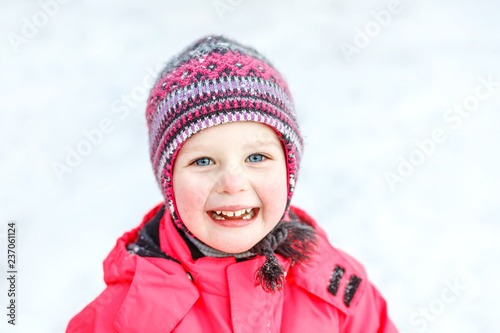 A pretty white girl in a knitted winter hat and pink jumpsuit, smiling and laughing in the snow . Portrait close-up. © Елена Нестерова