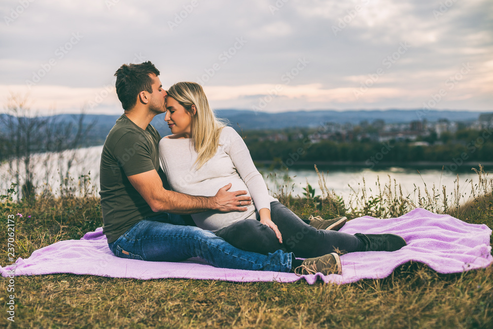 Husband kissing his pregnant wife into forehead and enjoy spending time together outdoor.