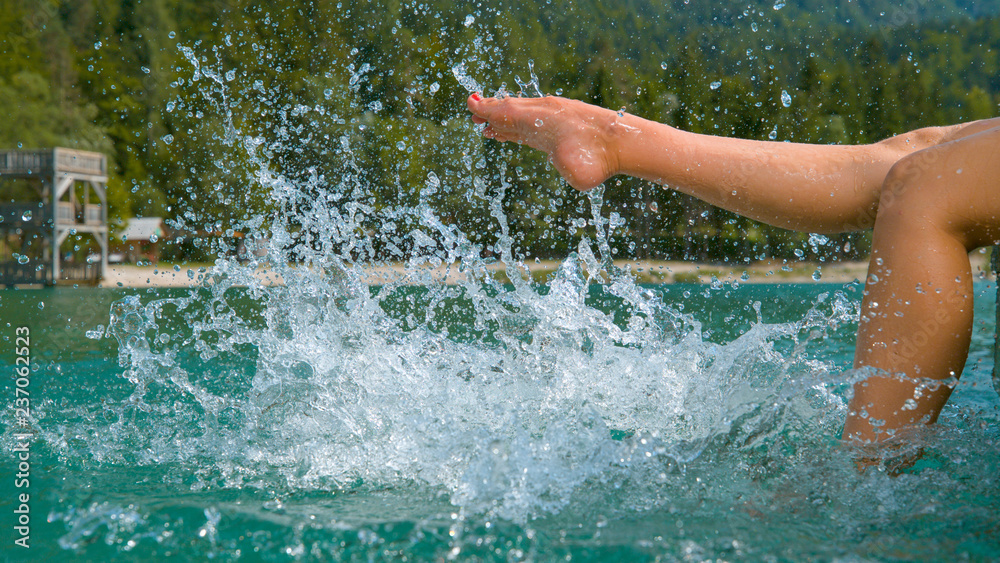 CLOSE UP: Unrecognizable playful girl kicking and splashing emerald lake water.