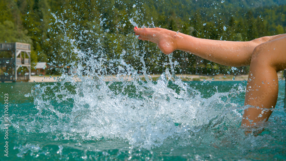 Fototapeta premium CLOSE UP: Unrecognizable playful girl kicking and splashing emerald lake water.