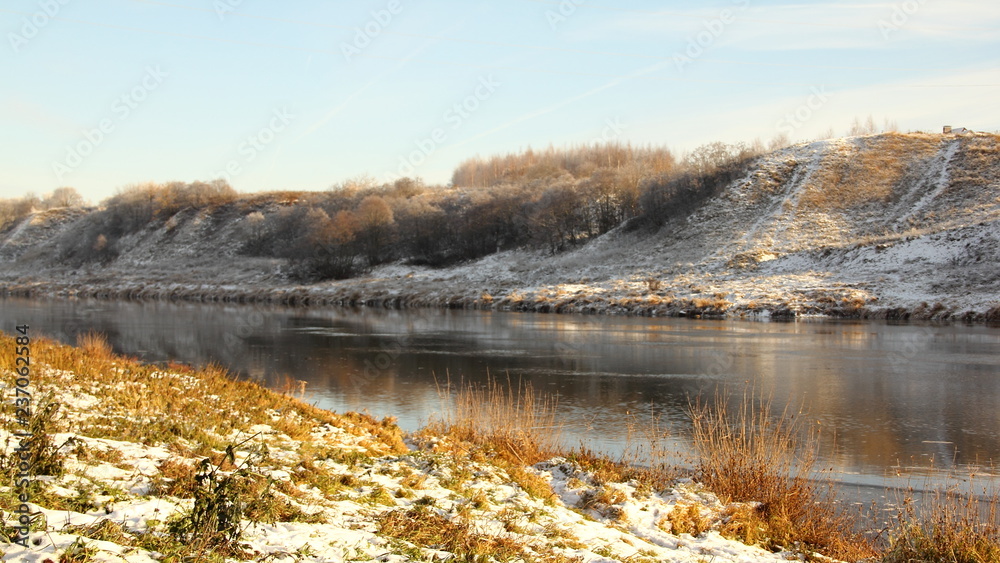 European river with a high Bank in the afternoon at the beginning of winter against the forest covered with frost on the horizon - the first snow, frost, panoramic beautiful water landscape European river with a high Bank in the afternoon at the beginning of winter against the forest covered with frost on the horizon - the first snow, frost, panoramic beautiful water landscape