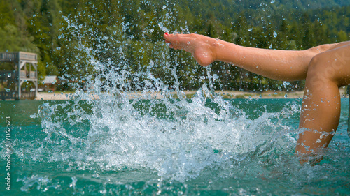 CLOSE UP: Unrecognizable playful girl kicking and splashing emerald lake water.