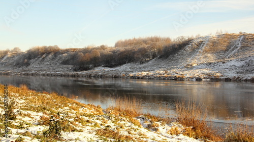 European river with a high Bank in the afternoon at the beginning of winter against the forest covered with frost on the horizon - the first snow  frost  panoramic beautiful water landscape