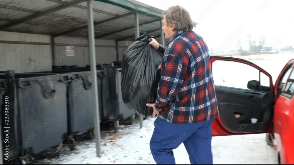 Man throws a black bag with of garbage in the trash. From the red passenger car. Man throws a black bag with of garbage in the trash. From the red passenger car.