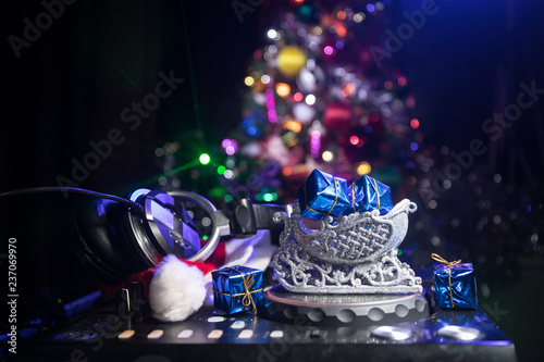 Dj mixer with headphones on dark nightclub background with Christmas tree New Year Eve. Close up view of New Year elements on a Dj table. Holiday party concept.