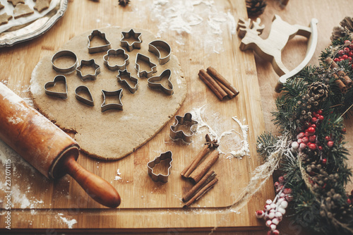 Christmas gingerbread cookies dough with metal cutters on rustic table with wooden rolling pin, cinnamon ,anise, cones, christmas decorations. Atmospheric stylish image, winter holidays