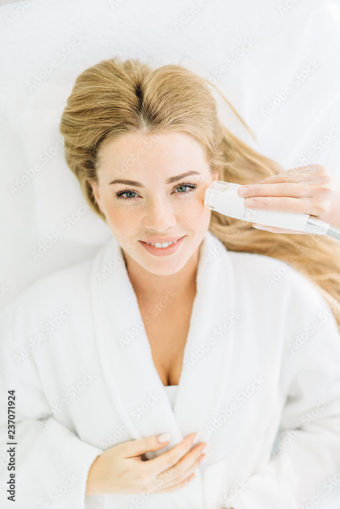Beautiful blonde woman with gorgeous long hair and perfect skin makes face laser resurfacing, top view. Skin pore cleansing. Anti-aging treatments. Spa. Non-invasive therapy Beautiful blonde woman with gorgeous long hair and perfect skin makes face laser resurfacing, top view. Skin pore cleansing. Anti-aging treatments. Spa. Non-invasive therapy