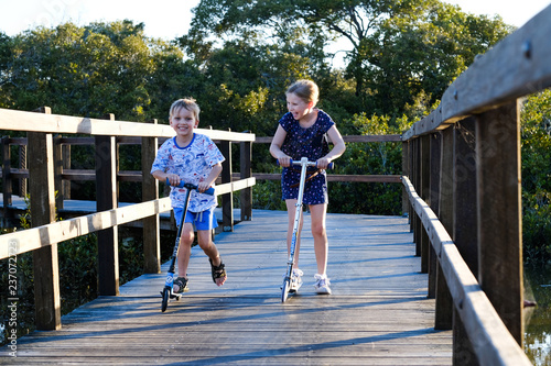 Sister and brother ride their scooters on a boardwalk in Brisbane, Australia