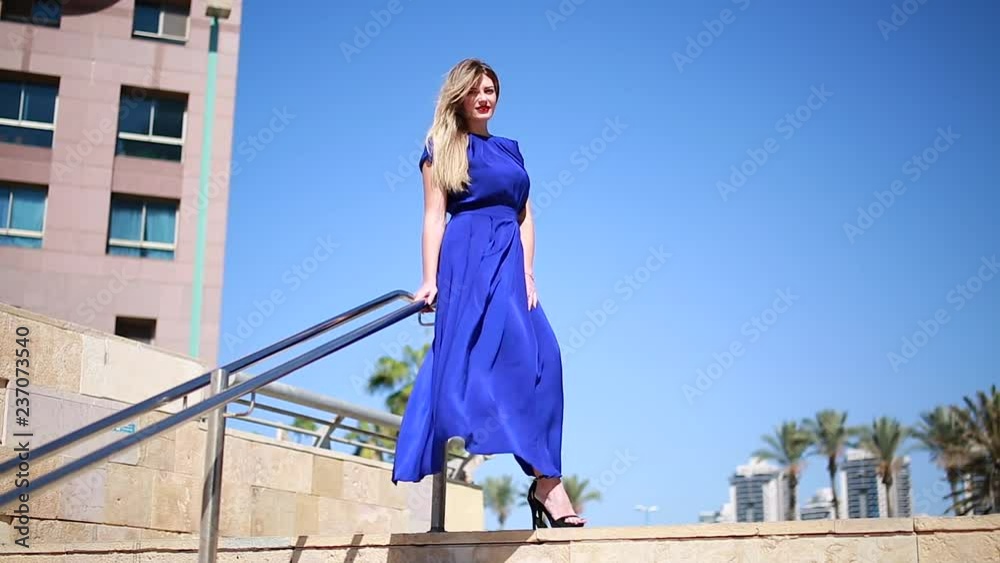 A woman with long hair and a blue dress comes down the steps, and the wind blows