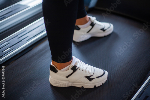Close-up of feet of young woman in sportswear is running on a treadmill in the gym