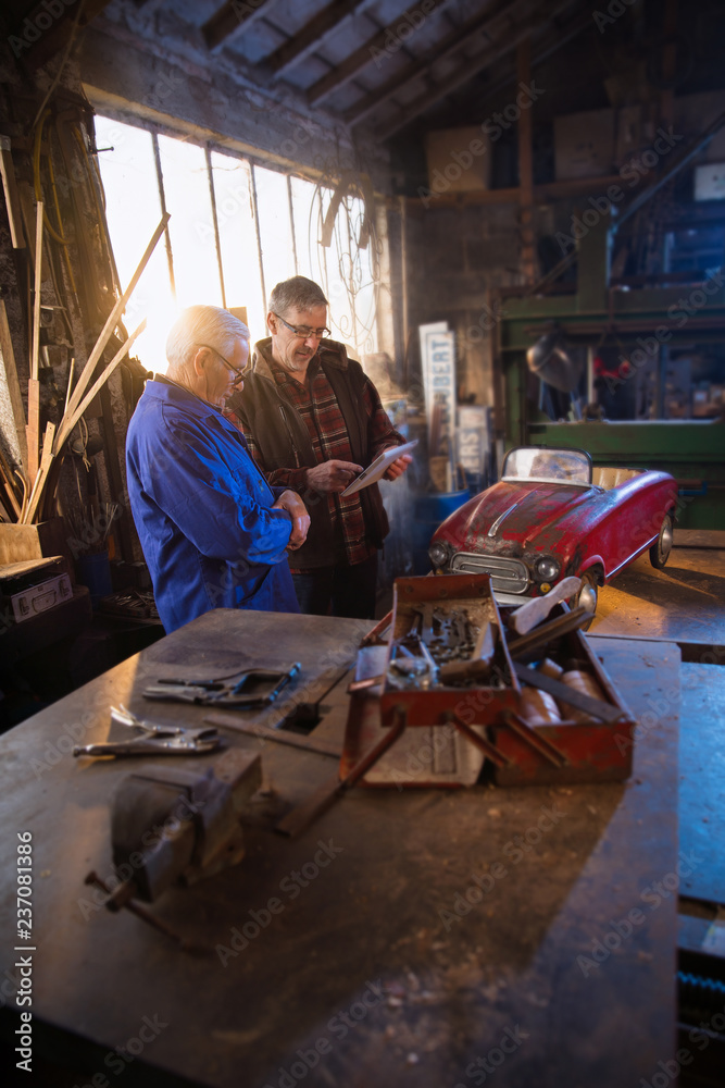 A senior man and his son at workshop to restore an old pedal car A senior man and his son at workshop to restore an old pedal car