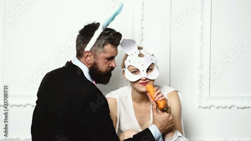 Bearded man in a suit feed woman by carrot who is dressed in a leather mask on white background. Fashion concept. photo