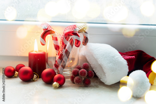 Christmas scene with burning candle, sanra claus hat and decorations on winter windowsill with bokeh lights photo