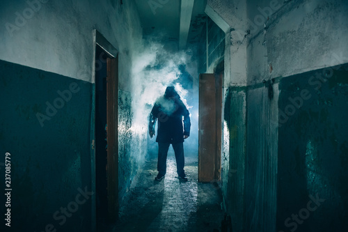 Dark silhouette of strange danger man in hood in back light with smoke or fog in scary grunge corridor or tunnel