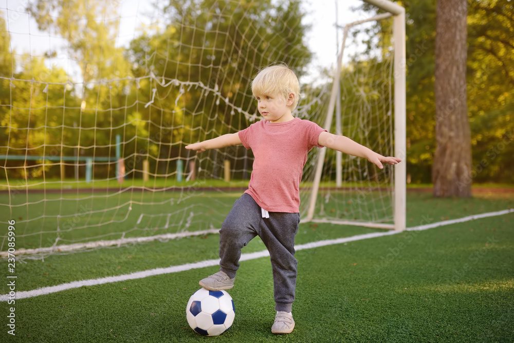 Little boy having fun playing a soccer/football game on summer day. Active outdoors game/sport for children. Little boy having fun playing a soccer/football game on summer day. Active outdoors game/sport for children.